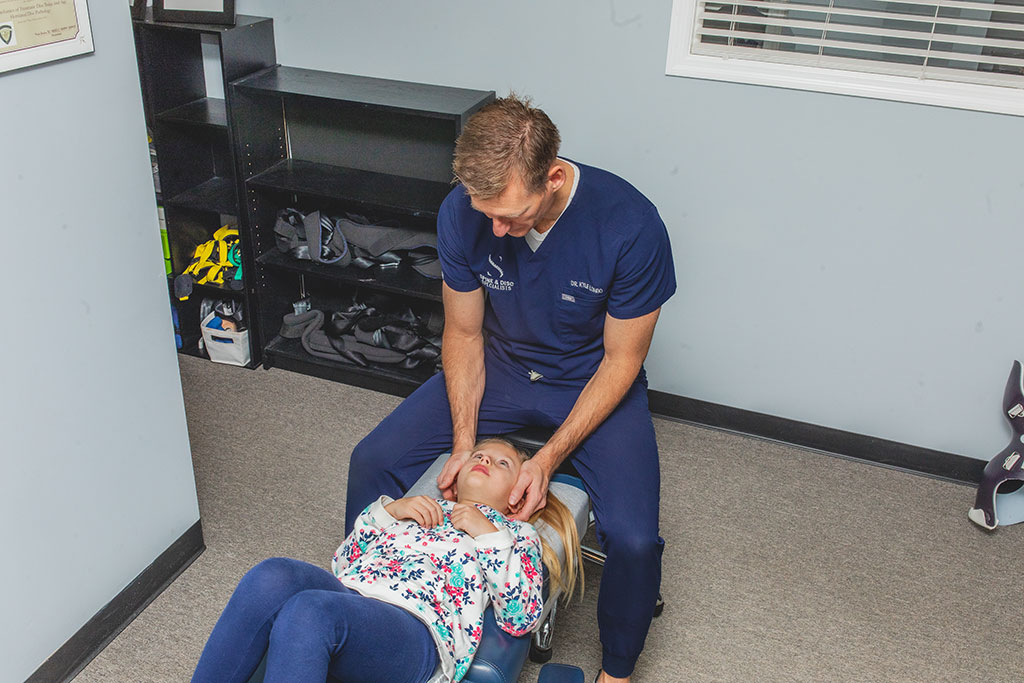 Dr. Longo adjusting a young girl's neck as part of chiropractic neck pain treatment
